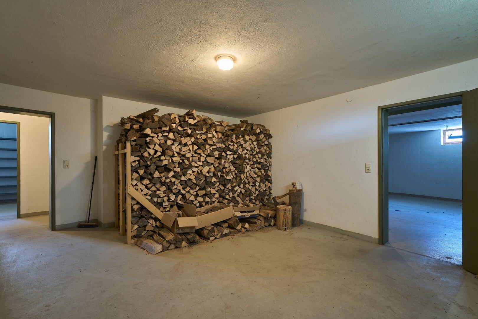 Kellerraum mit gestapeltem Brennholz und Zugang zu weiteren Räumen.