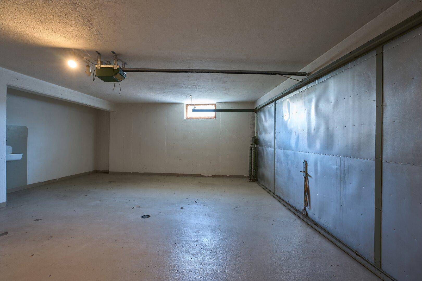 Geräumige Garage mit Betonboden und automatischem Tor, bietet Platz für Fahrzeuge.