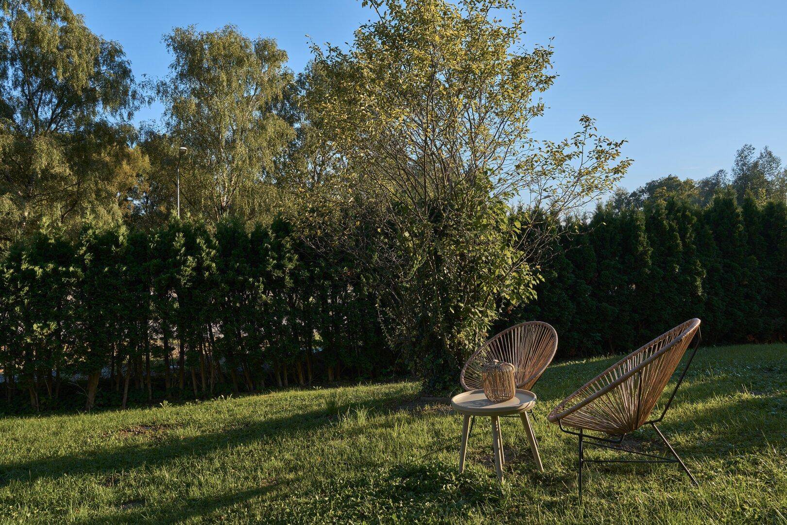 Gartenbereich mit zwei modernen Stühlen und einem kleinen Tisch, umgeben von üppigem Grün.