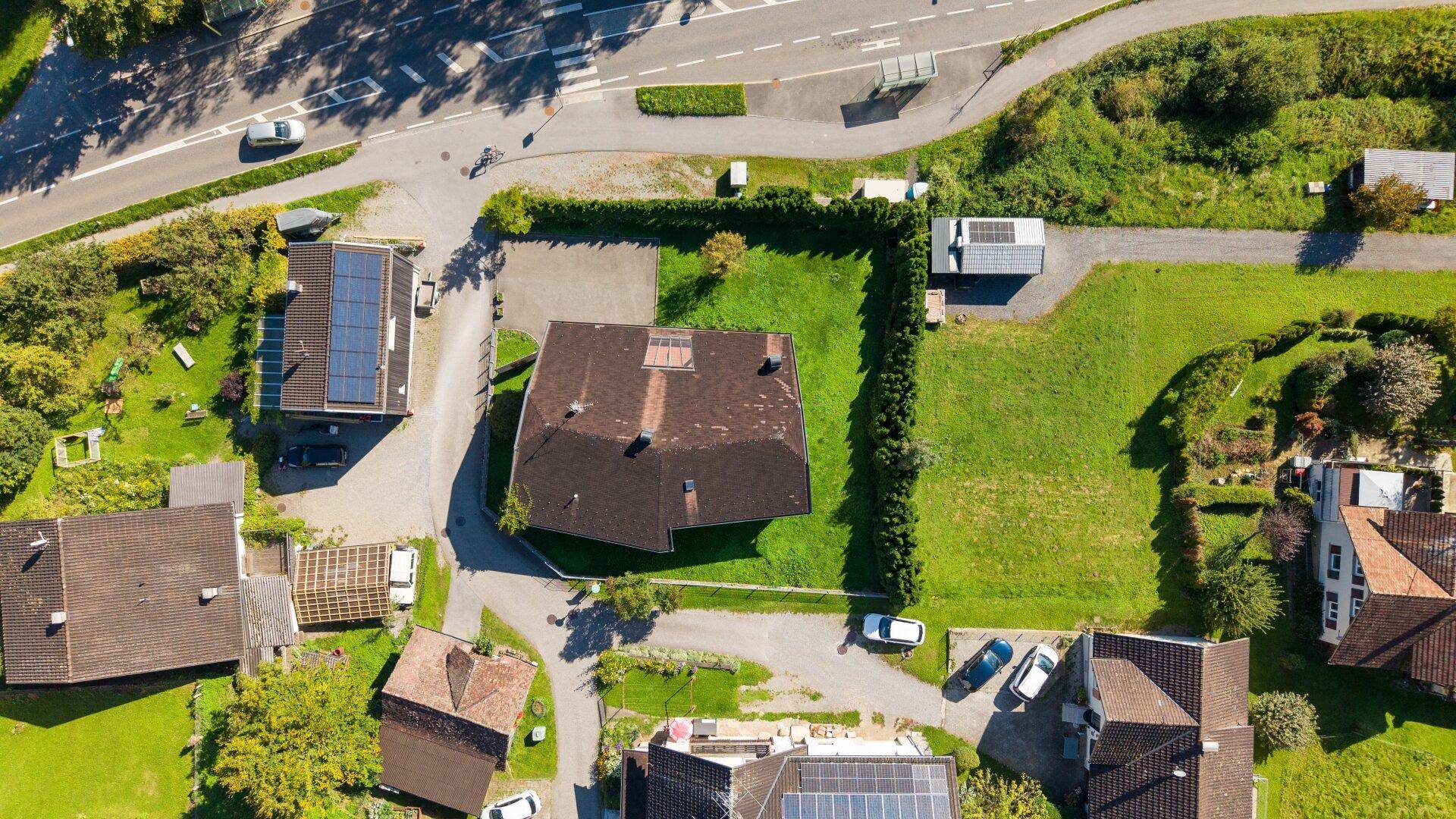 Luftaufnahme eines Einfamilienhauses mit großem Garten, umgeben von Nachbarhäusern und einer Straße.