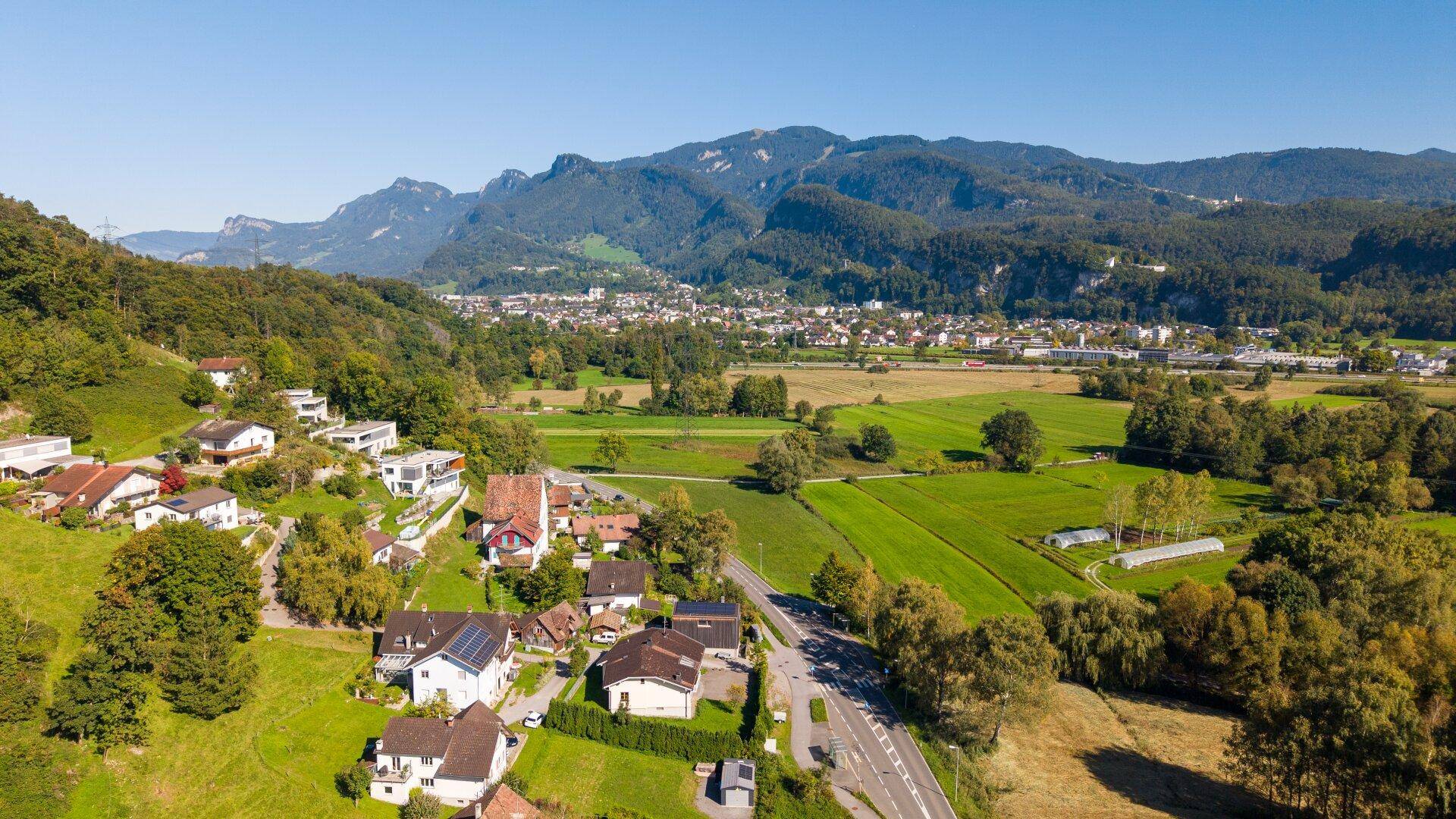 Weitläufige Luftaufnahme eines Tals mit Siedlungen, Feldern und einer beeindruckenden Bergkulisse.