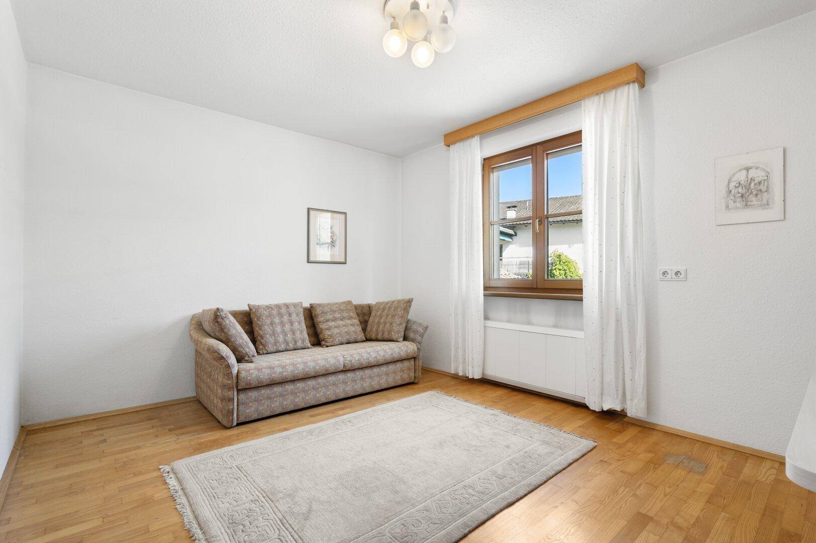 Gemütlicher Raum mit Holzboden, Sofa und Fenster, ideal als Gäste- oder Wohnzimmer.