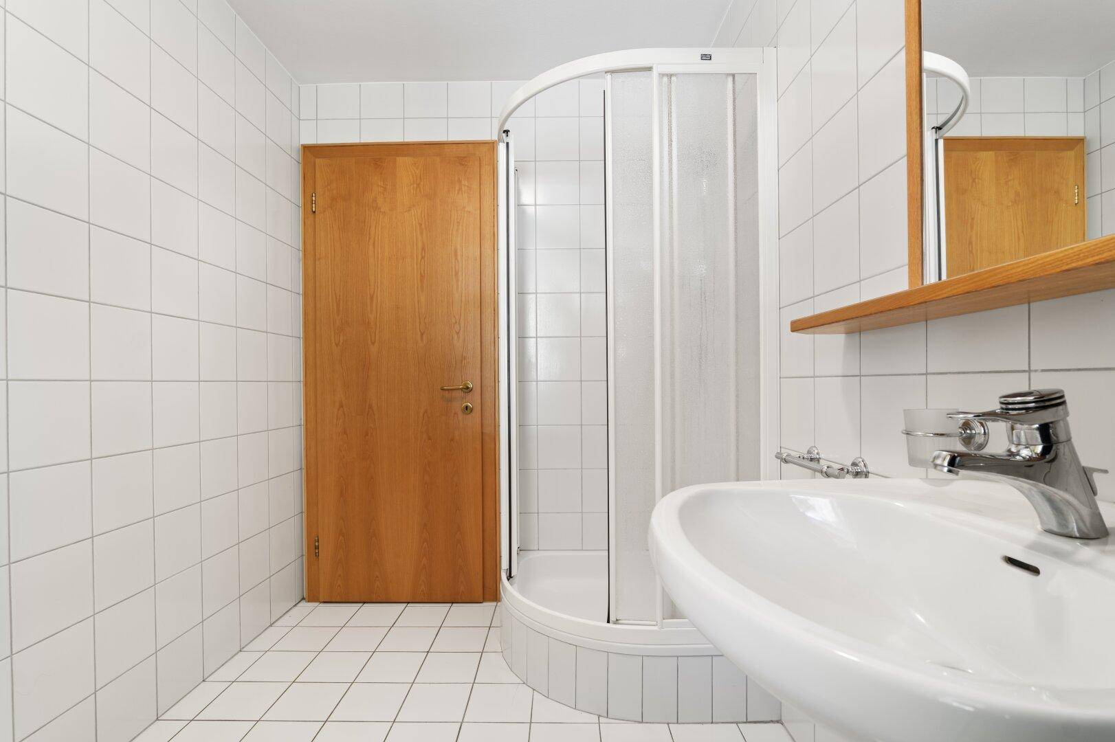 Badezimmer mit weißen Fliesen, Waschbecken und einer praktischen Duschkabine.