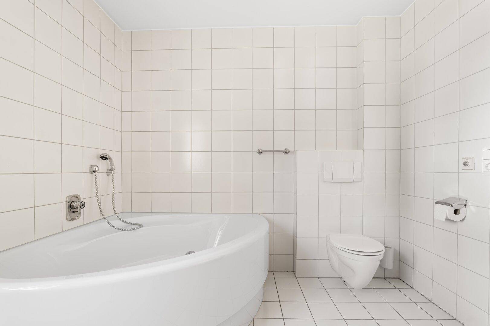 Badezimmer mit weißen Fliesen, einer Badewanne und einer wandhängenden Toilette.