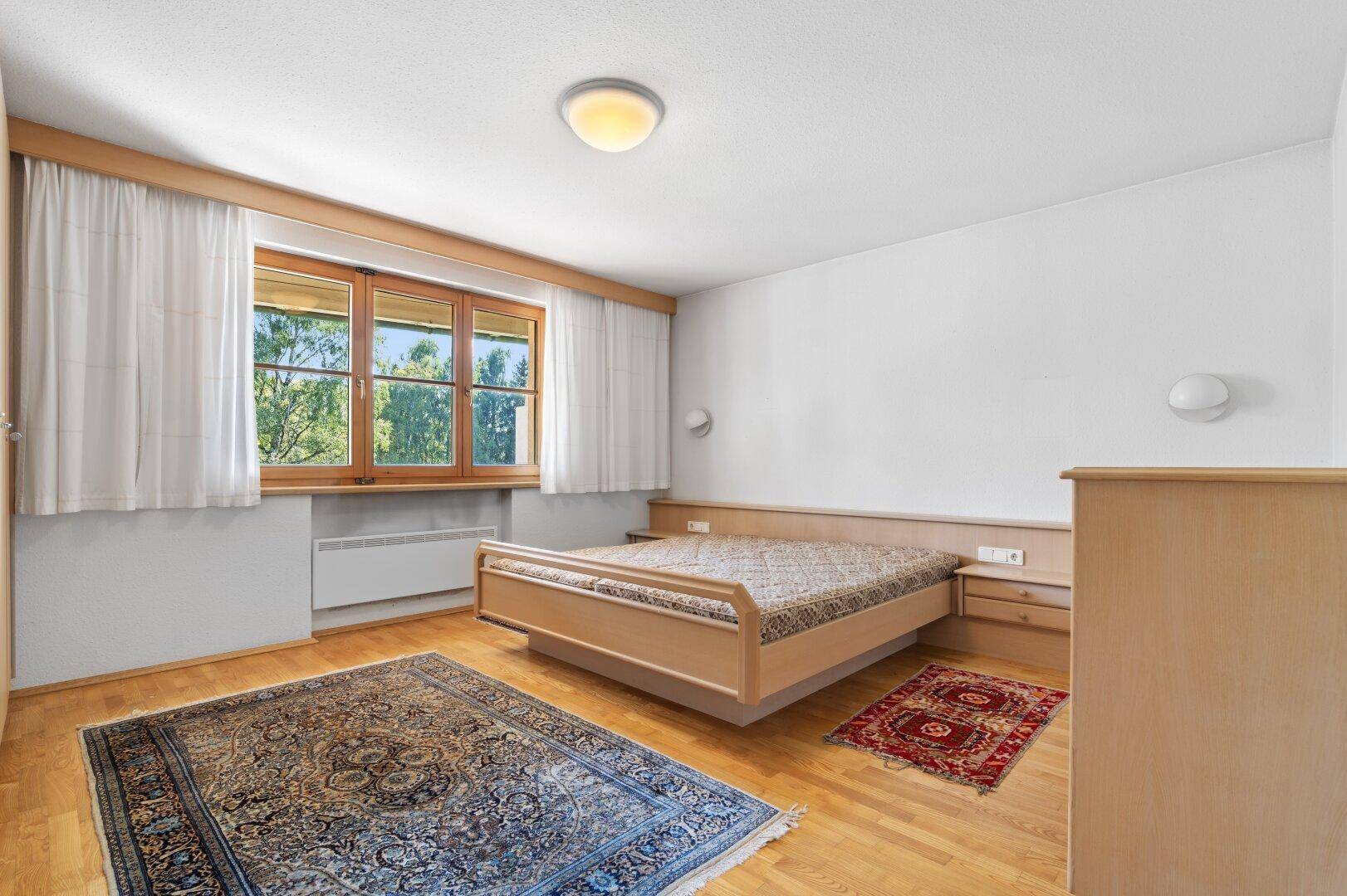 Helles Schlafzimmer mit Holzboden, Doppelbett und Fenster mit Blick ins Grüne.
