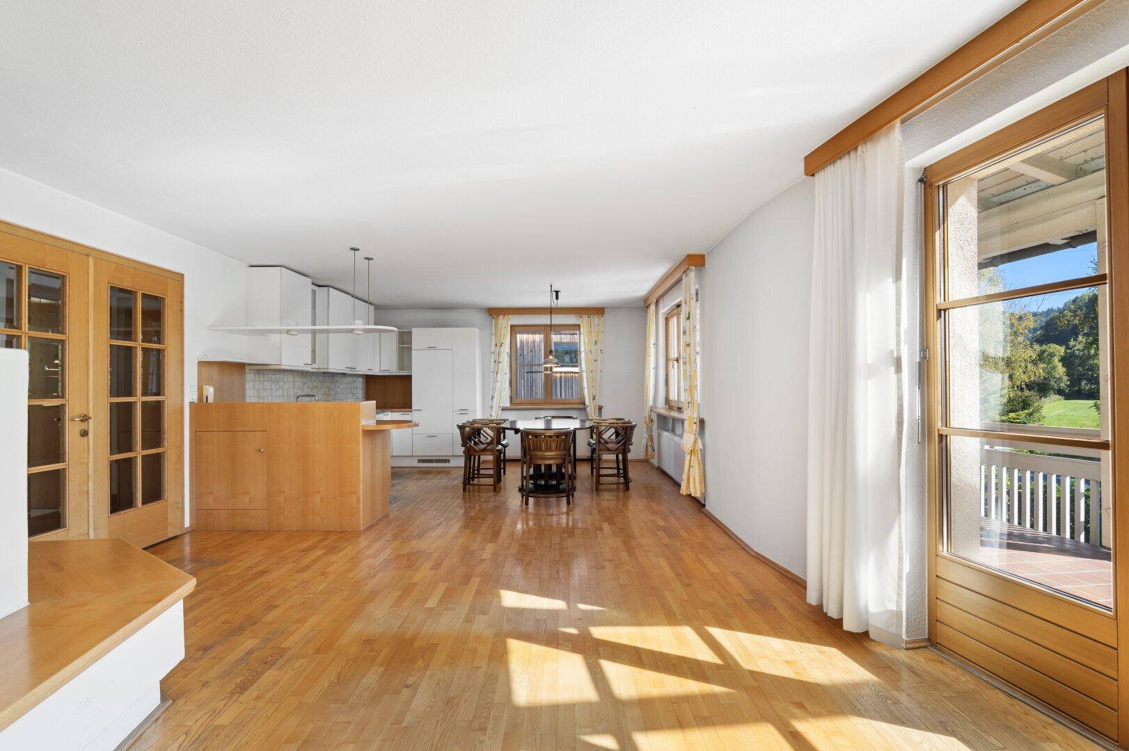Offener Wohn- und Essbereich mit Holzboden und direktem Zugang zum Balkon.