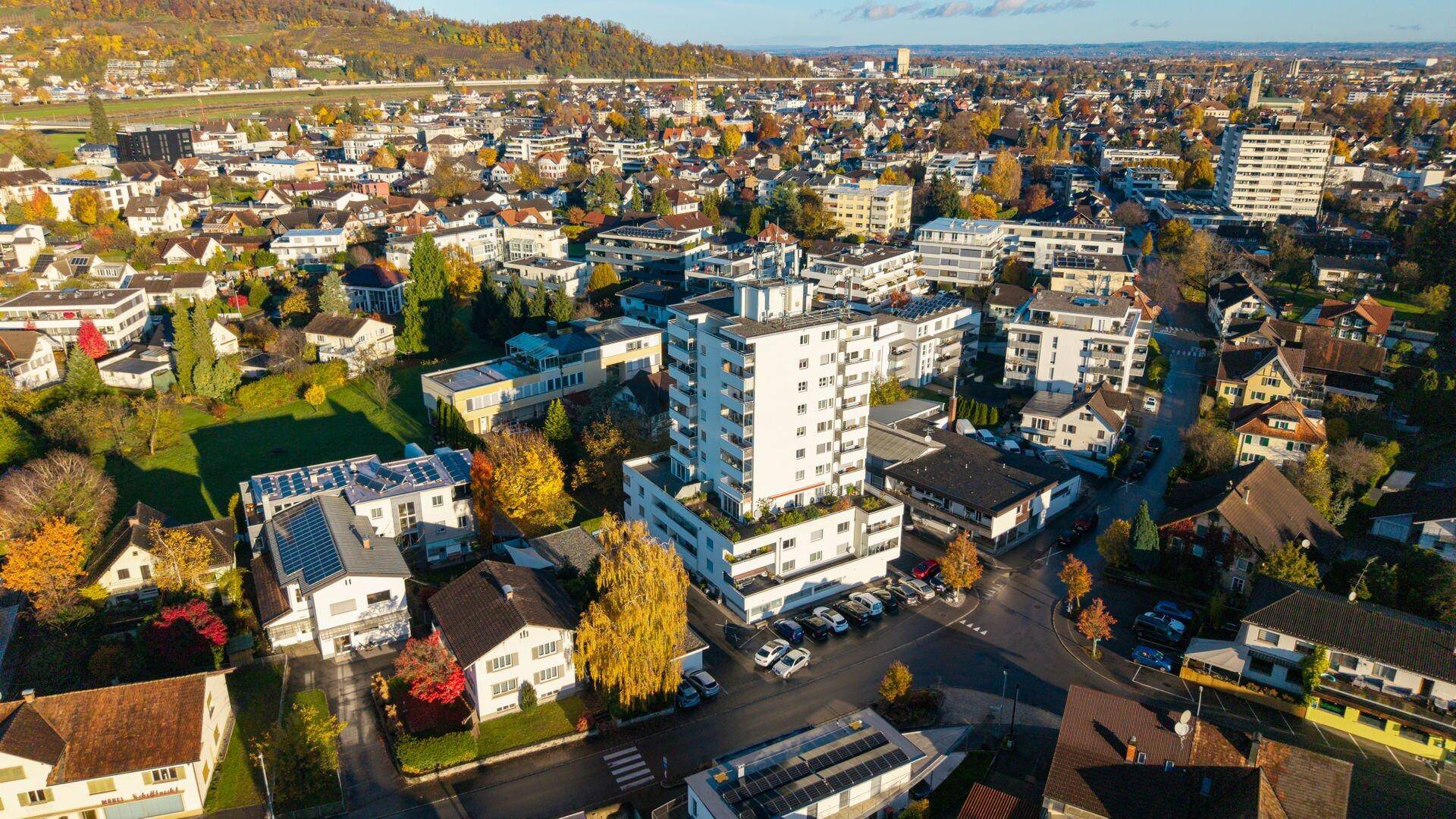 Weitläufige Luftaufnahme des Wohngebäudes und der umliegenden Siedlung mit herbstlicher Vegetation.