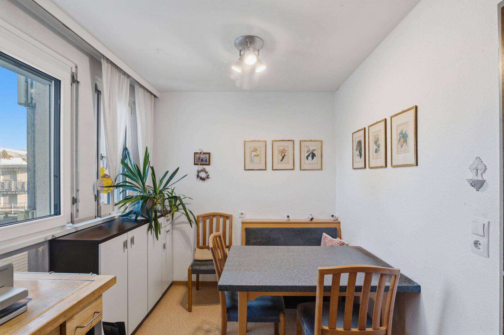 Essbereich mit Holztisch, Stühlen und einer Sitzbank, beleuchtet durch ein großes Fenster.