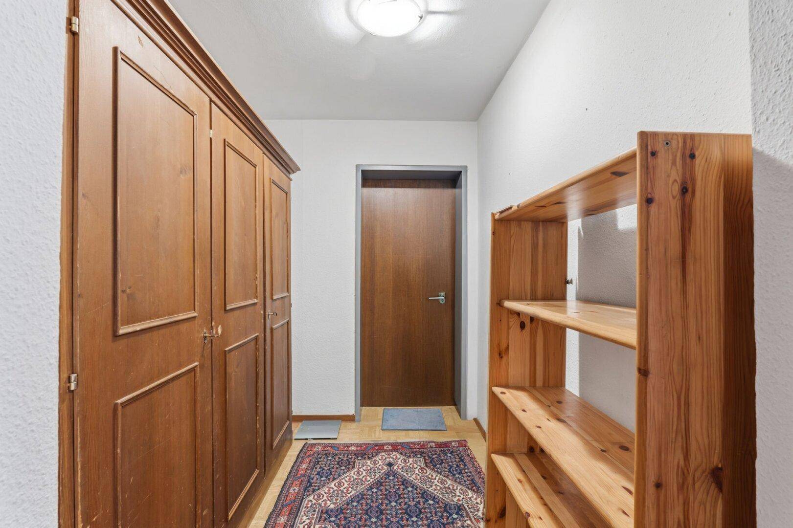 Eingangsbereich mit Holzschrank, Regal und Teppichläufer auf hellem Holzboden.