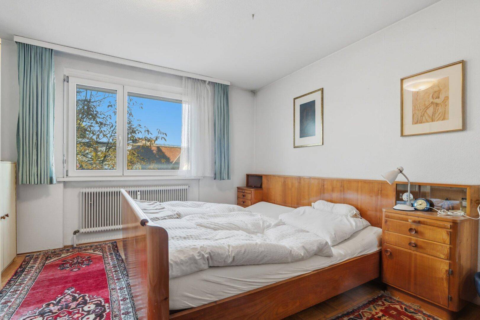 Schlafzimmer mit Doppelbett, Holzmöbeln und Fenster mit Blick ins Grüne.
