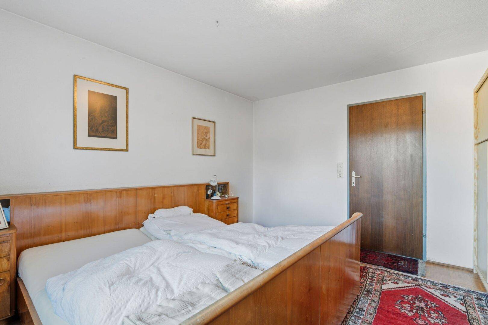Schlafzimmer mit klassischem Holzbett und passenden Nachttischen, Teppich auf Holzboden.