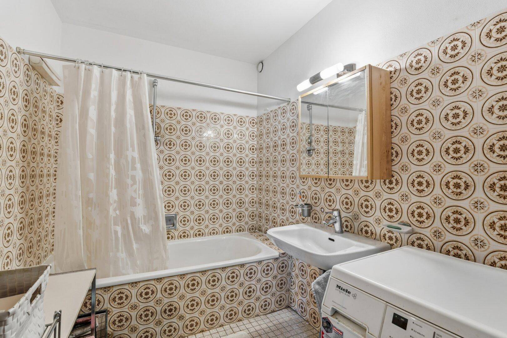 Badezimmer mit Badewanne, Waschbecken und gemusterten Fliesen im Retro-Stil.
