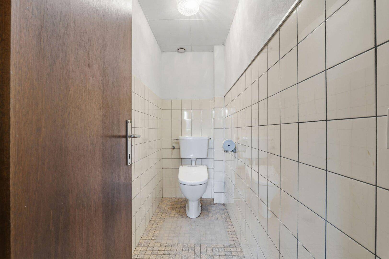 Separate Toilette mit weißen Fliesen und einfacher Ausstattung.