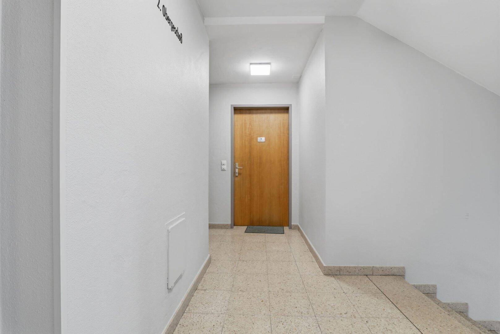 Heller Hausflur mit Terrazzoboden und Zugang zu den Wohnungen im Obergeschoss.