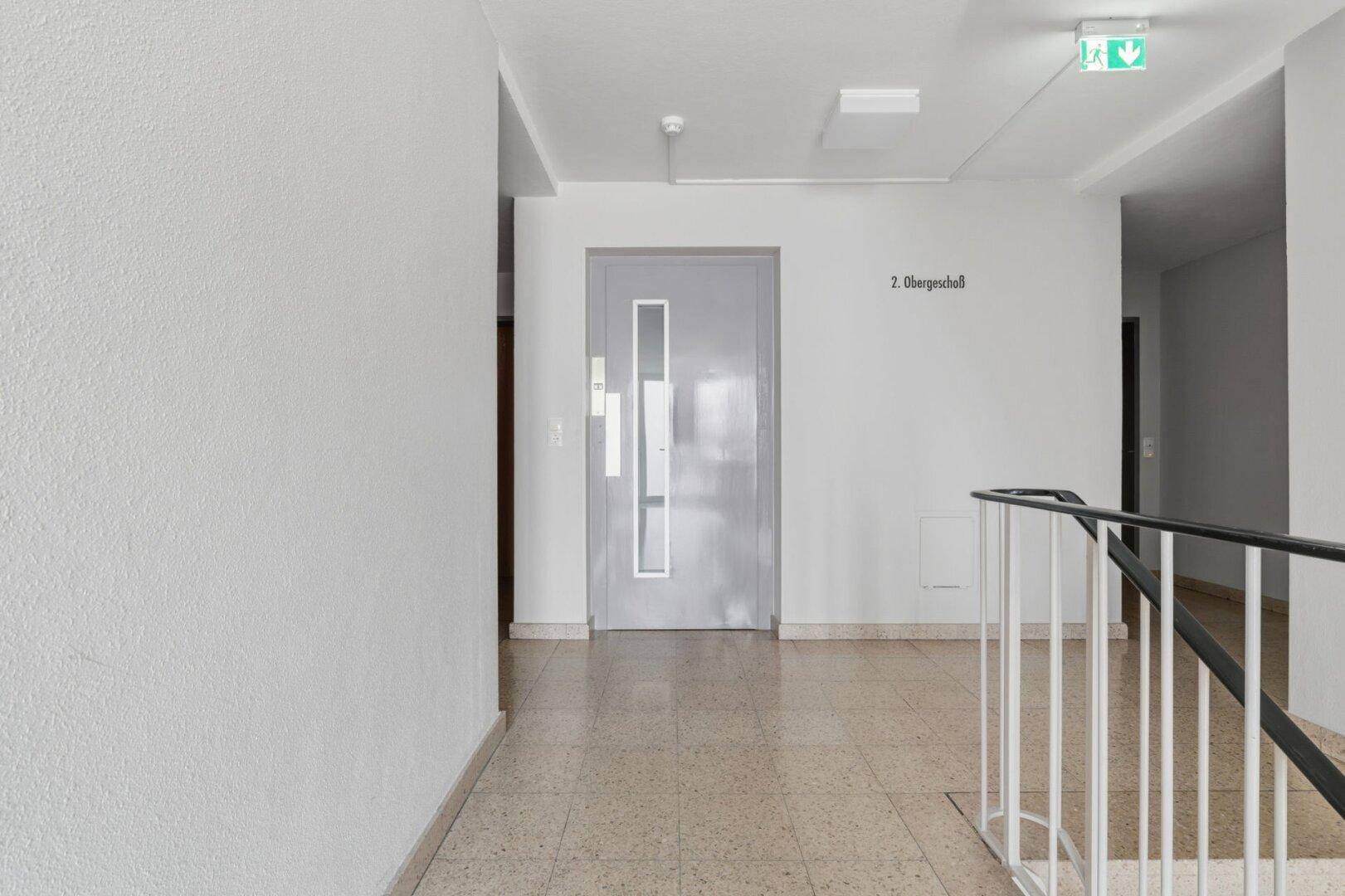 Gemeinschaftlicher Flur im Obergeschoss mit heller Tür und Treppenaufgang.