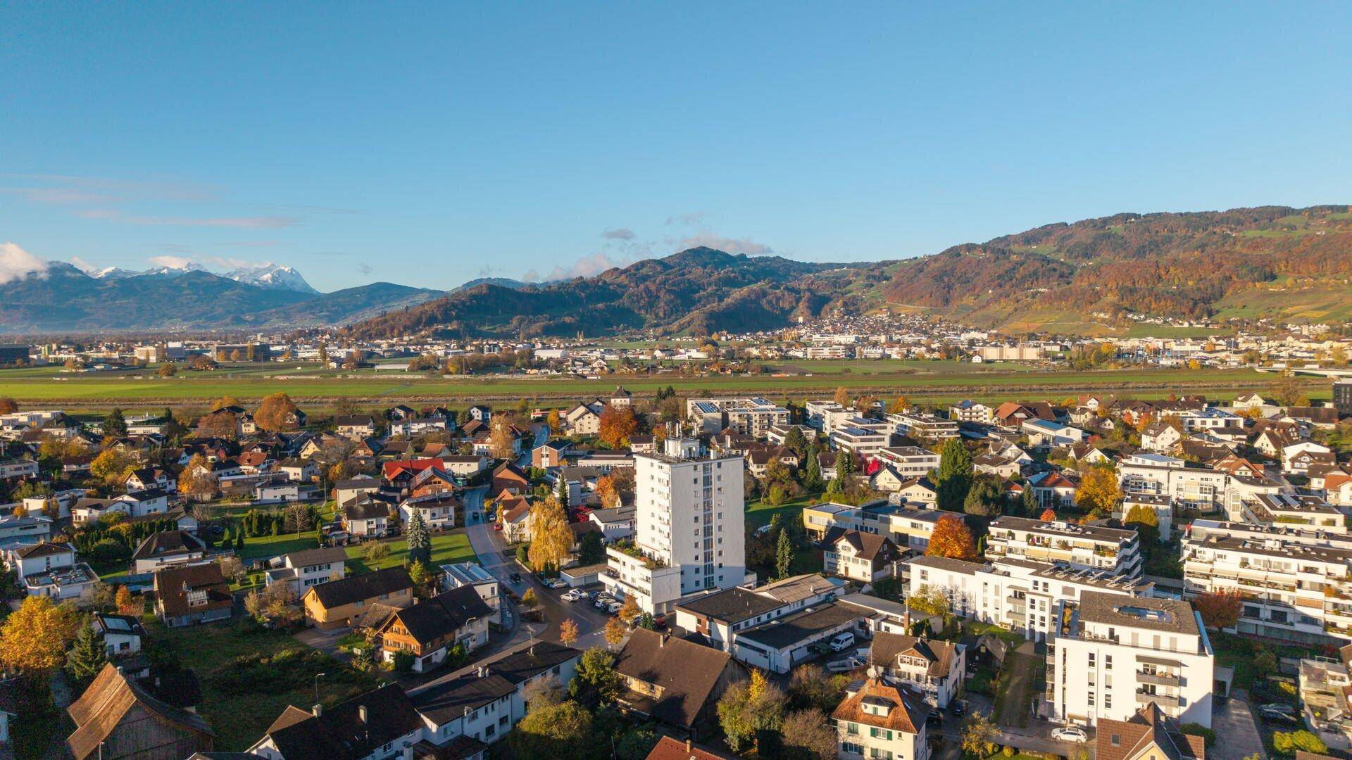 Weitwinkelaufnahme der Wohngegend mit dem Hochhaus, umgeben von Hügeln und Feldern.