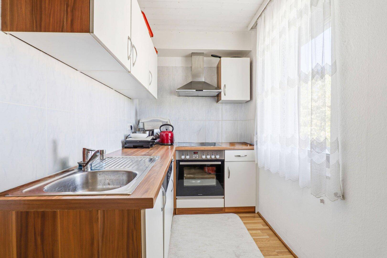 Schmale Küche mit Holz-Arbeitsplatten, weißen Schränken und einem Fenster für natürliches Licht.