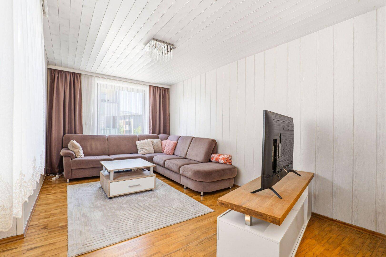 Geräumiges Wohnzimmer mit großem Ecksofa, Holzboden und hellem Teppich, ideal zum Entspannen.