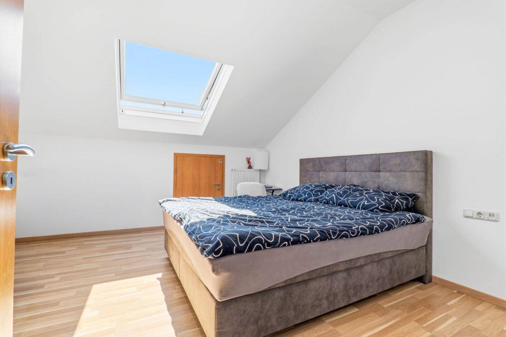 Helles Schlafzimmer im Dachgeschoss mit Doppelbett, Holzboden und einem großen Dachfenster.