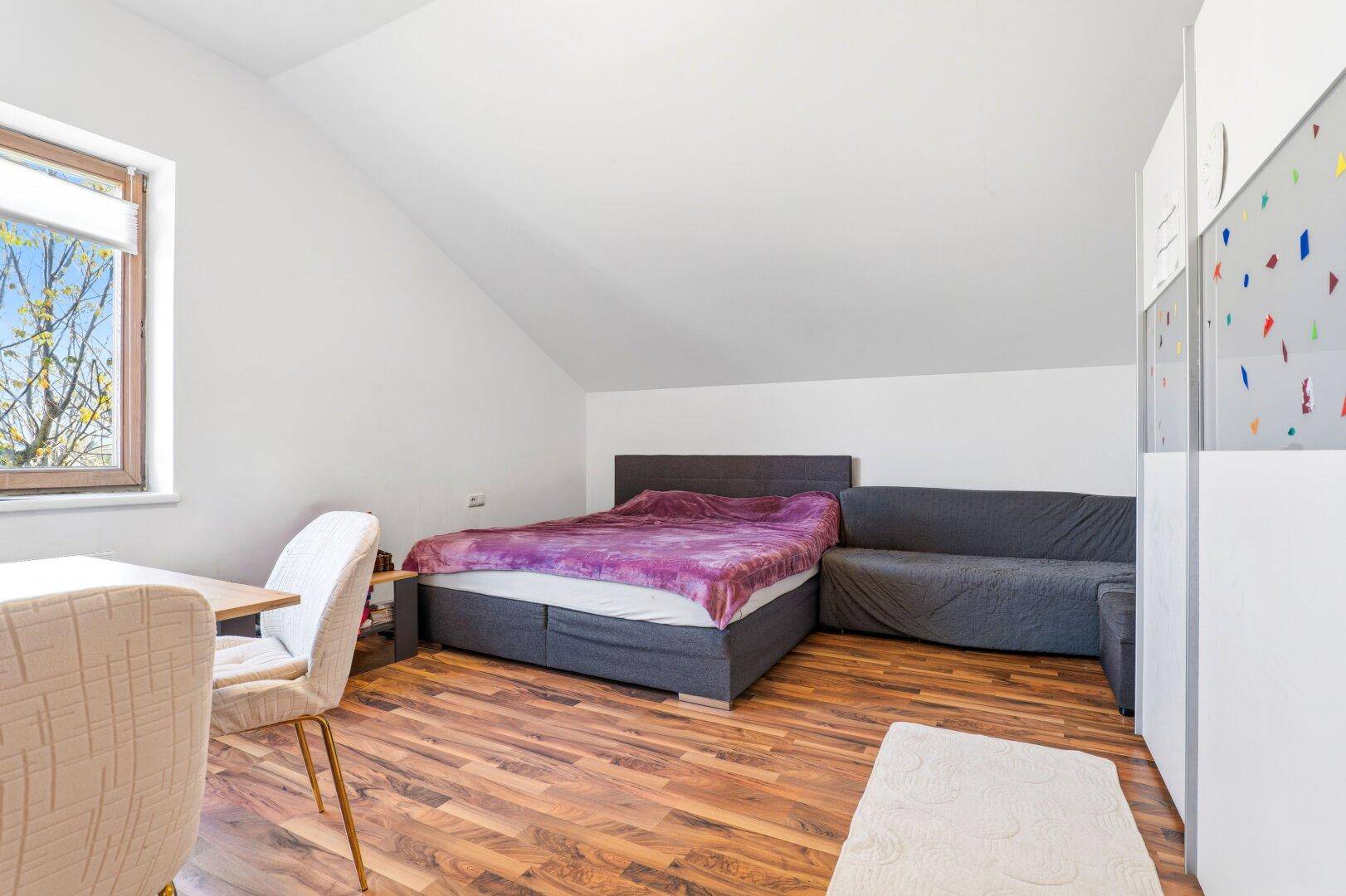 Gemütliches Schlafzimmer im Dachgeschoss mit Holzboden, Bett und einem Fenster, das Tageslicht spendet.