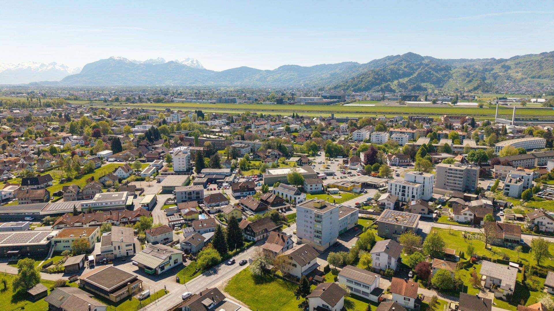 Panoramablick aus der Vogelperspektive auf eine Siedlung mit Bergen und weiten Landschaften unter blauem Himmel.