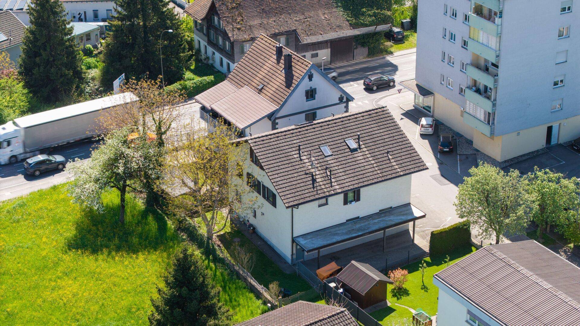 Überblick über das Wohngebiet mit einem Haus, Grünflächen und einer Straße mit vorbeifahrendem Verkehr.