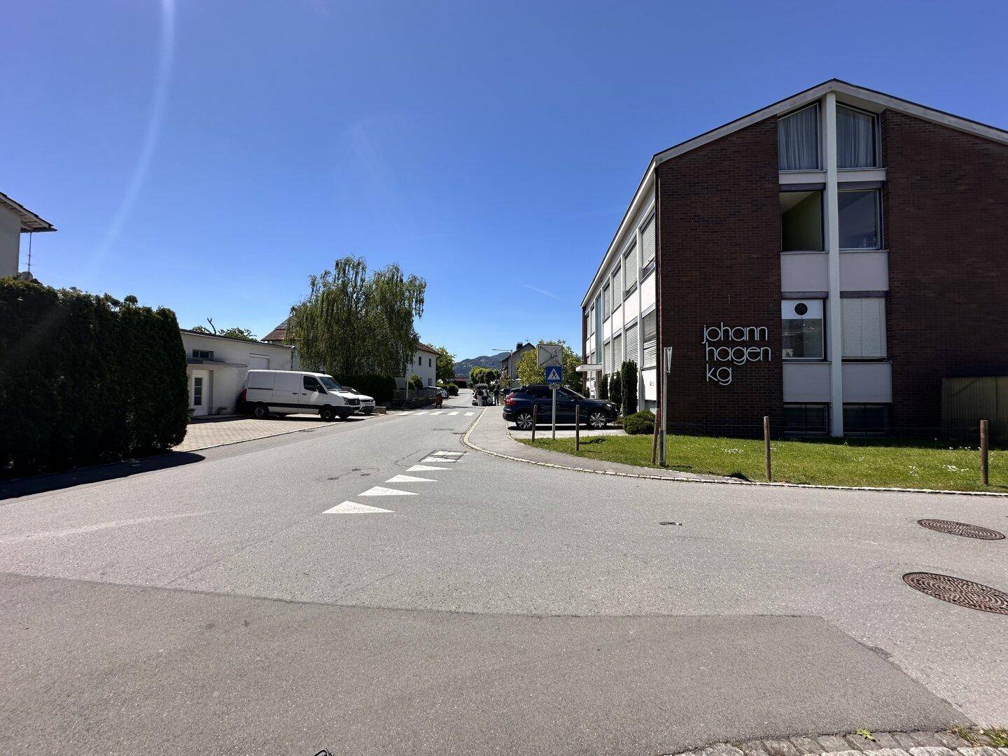 Außenansicht eines Backsteingebäudes an einer Straße mit geparkten Autos und Bäumen.