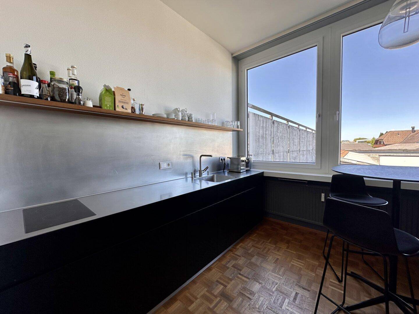 Kleine Teeküche mit schwarzer Arbeitsplatte, Spüle und einem Fenster mit Blick nach draußen.