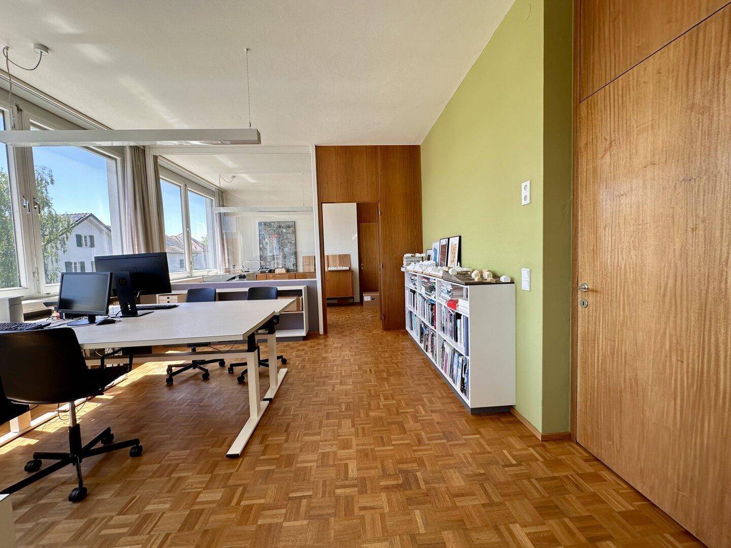 Helles Büro mit Holzvertäfelung, Bücherregal und mehreren Arbeitsplätzen.