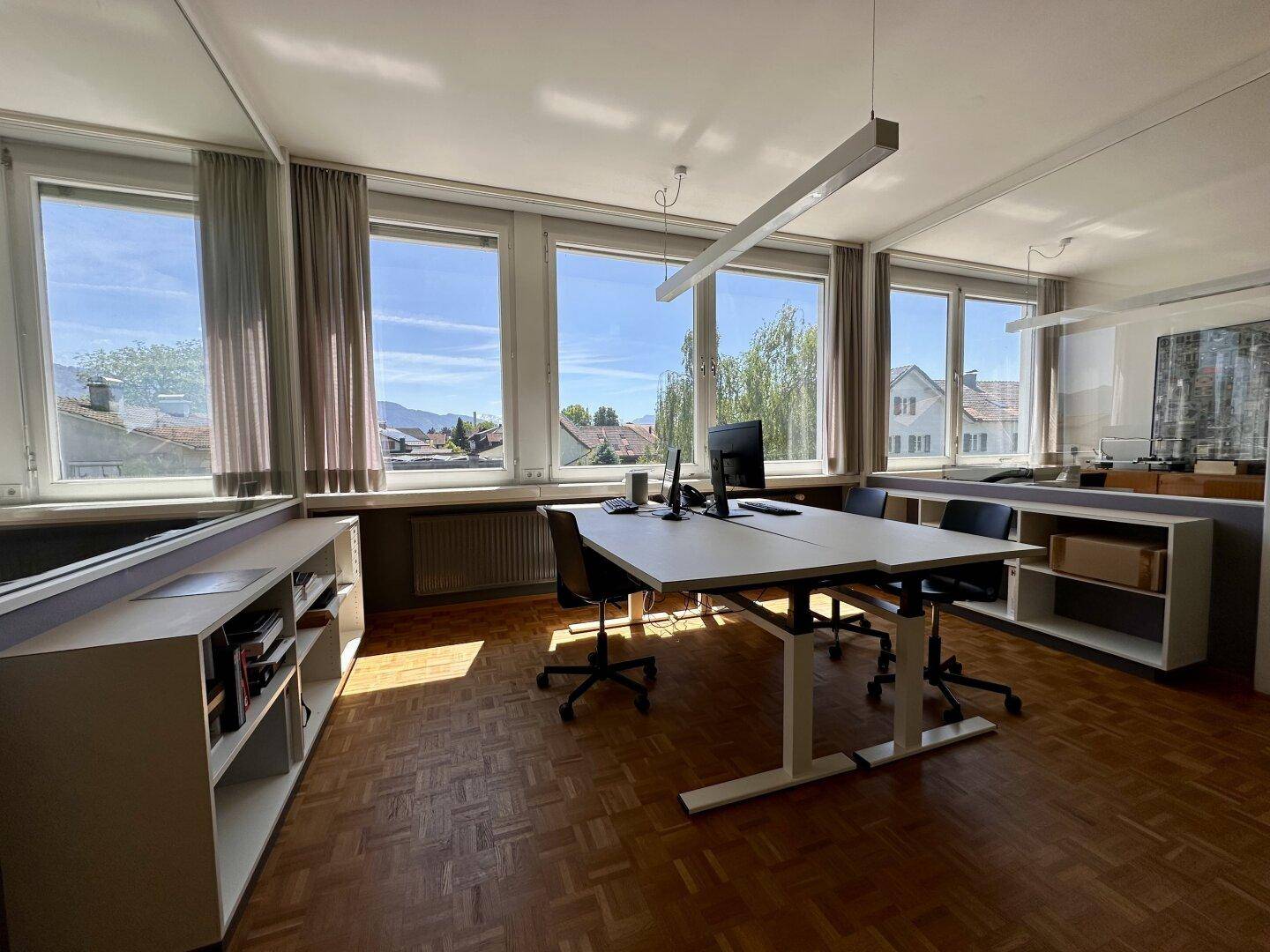 Modernes Büro mit mehreren Arbeitsplätzen, viel Tageslicht und Blick auf die Umgebung.