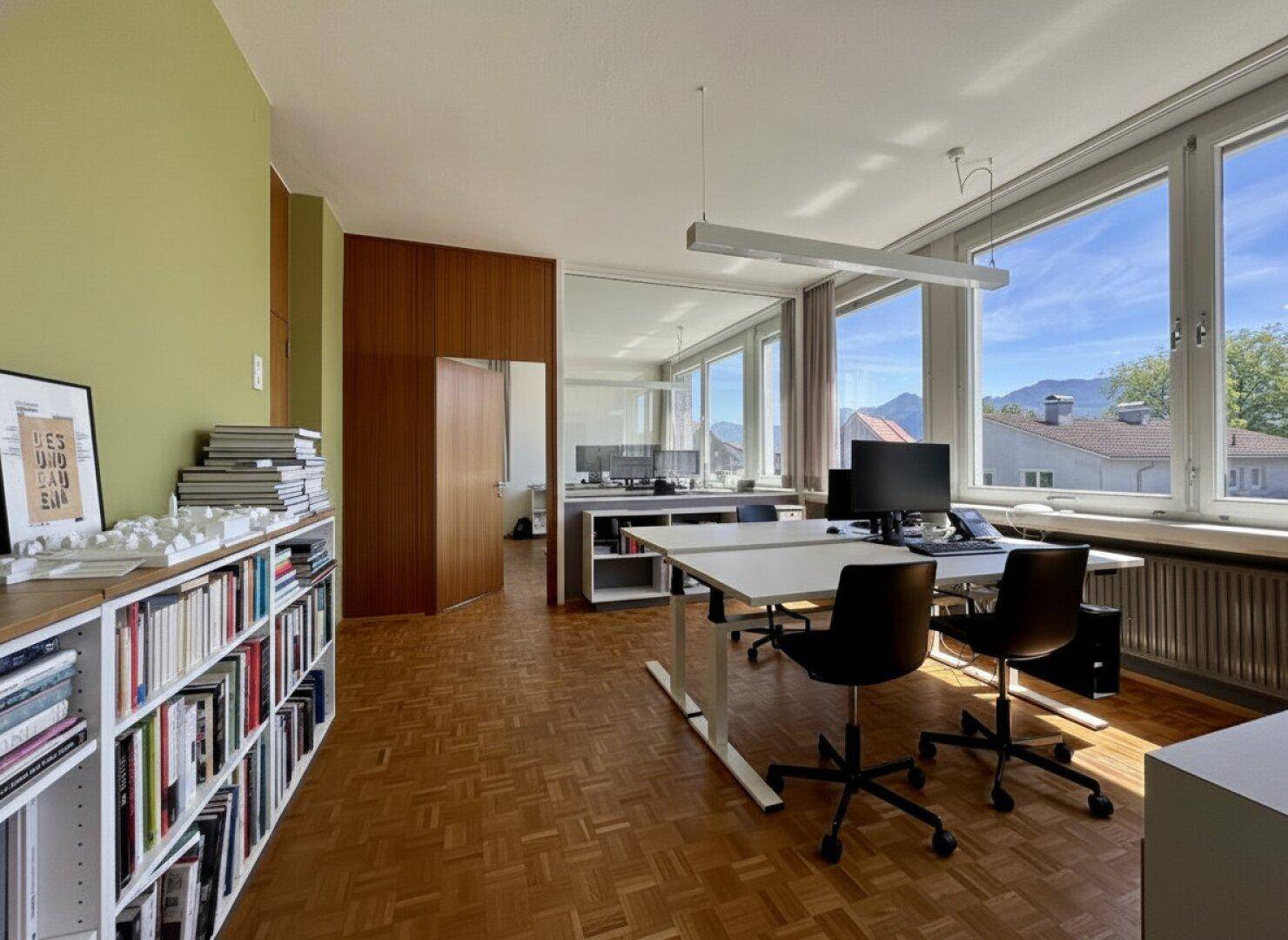 Geräumiges Büro mit mehreren Arbeitsplätzen, Bücherregalen und großen Fenstern mit Bergblick.