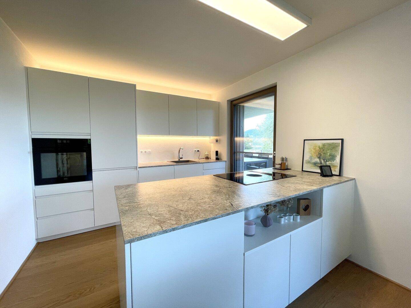 Moderne Einbauküche mit heller Arbeitsplatte, integrierten Geräten und Induktionskochfeld.