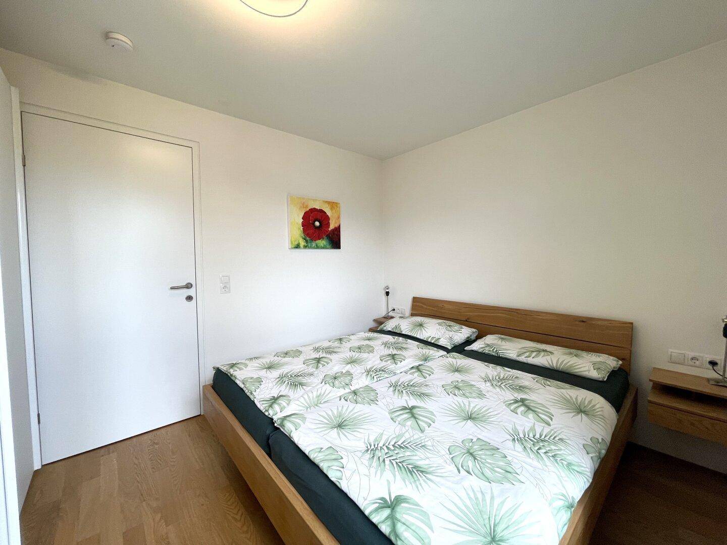Schlafzimmer mit Holzbett, Parkettboden und schlichter, heller Wandgestaltung.