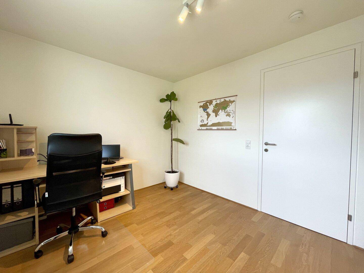 Helles Arbeitszimmer mit Schreibtisch, Bürostuhl und Parkettboden.