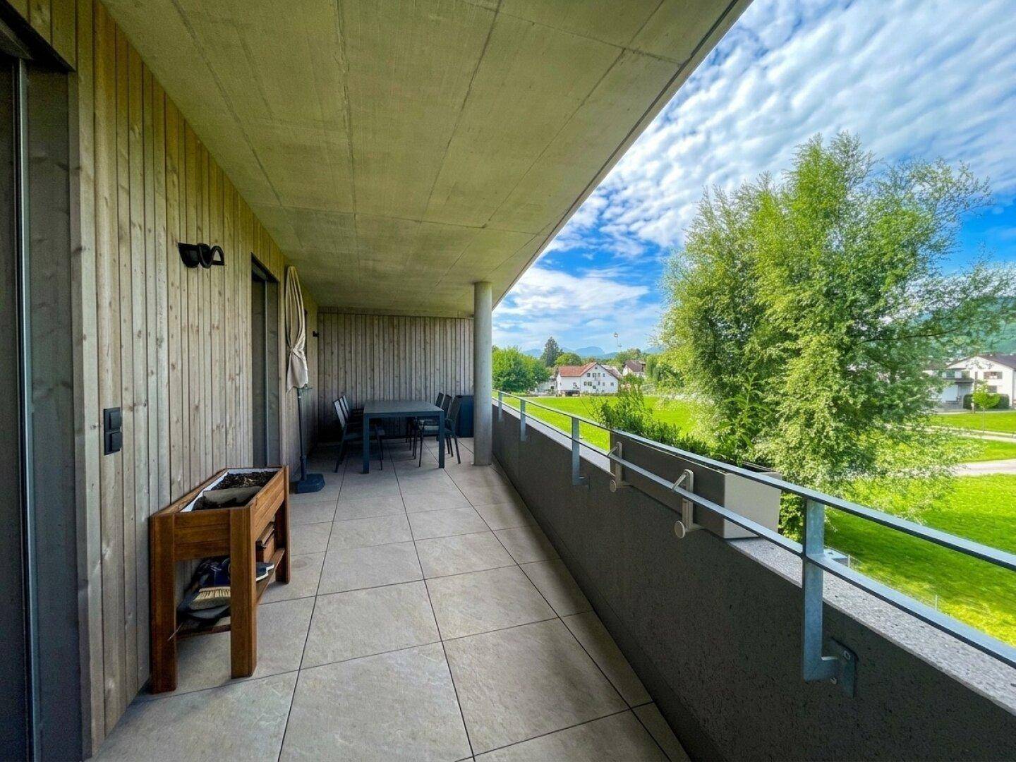 Geräumiger Balkon mit Fliesenboden, Esstisch und Blick ins Grüne.