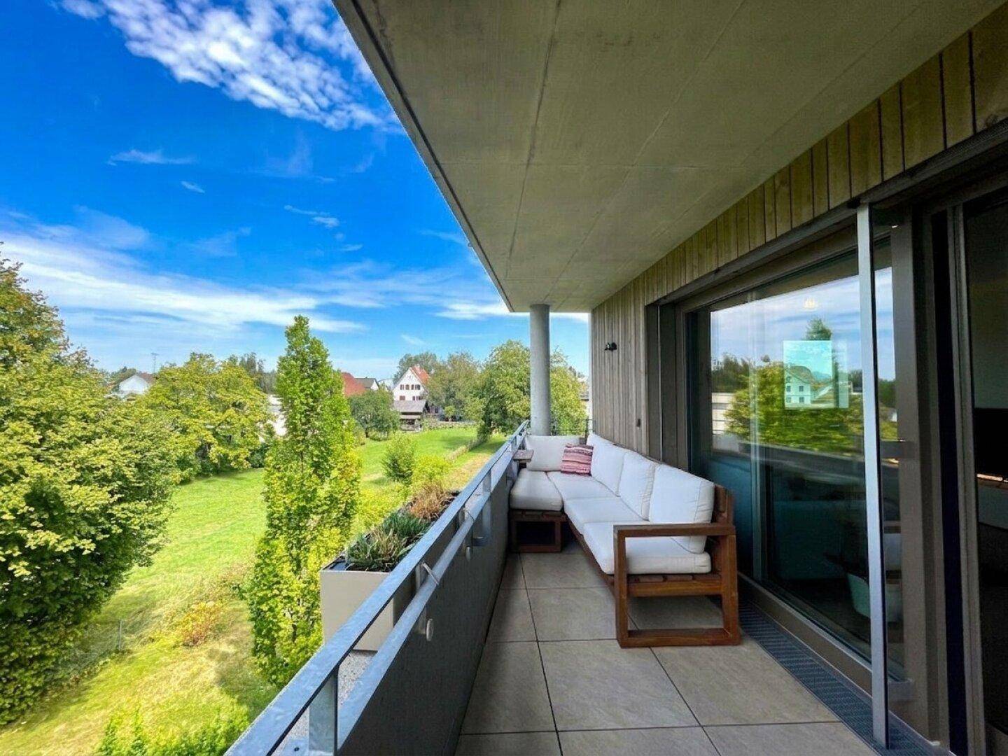 Großer Balkon mit Lounge-Möbeln, Fliesenboden und weitem Blick ins Grüne.