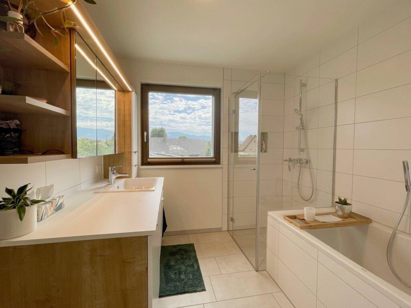 Modernes Badezimmer mit Badewanne, Dusche, Fenster und Waschtisch mit Holzunterschrank.