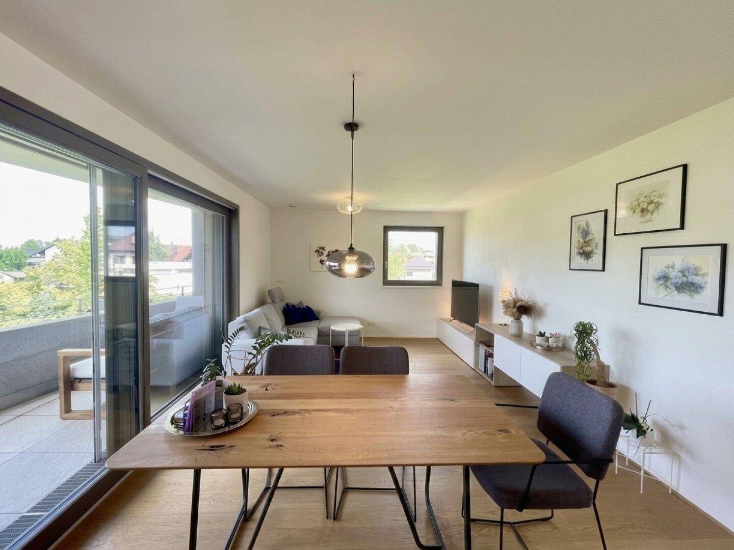 Geräumiger Wohn-Essbereich mit Holztisch, Sofa und Zugang zu einem großen Balkon.