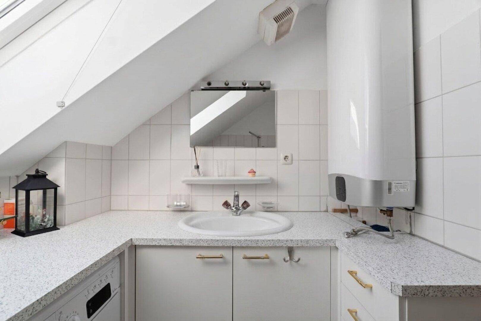 Helles Badezimmer im Dachgeschoss mit Waschbecken, weißen Fliesen und Warmwasserboiler unter Schräge.