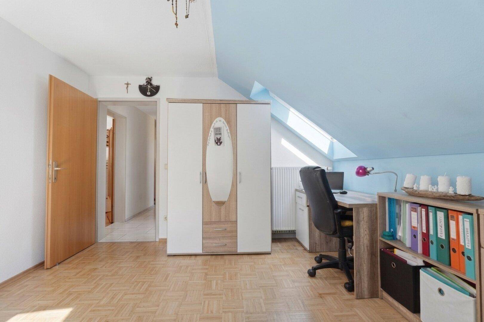 Dachzimmer, eingerichtet als Arbeitszimmer, mit Schreibtisch, Schrank und Dachschräge.