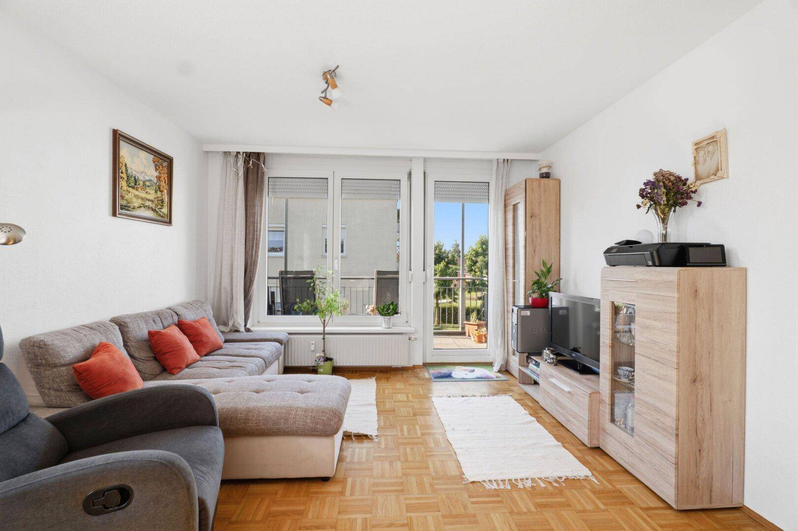 Helles Wohnzimmer mit Parkettboden, gemütlichem Sofa und Zugang zum Balkon.