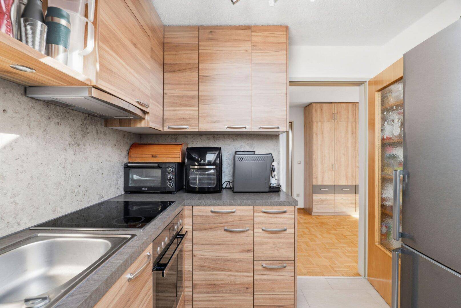 Funktionale Küche mit Holzschränken, dunkler Arbeitsplatte und modernen Geräten.