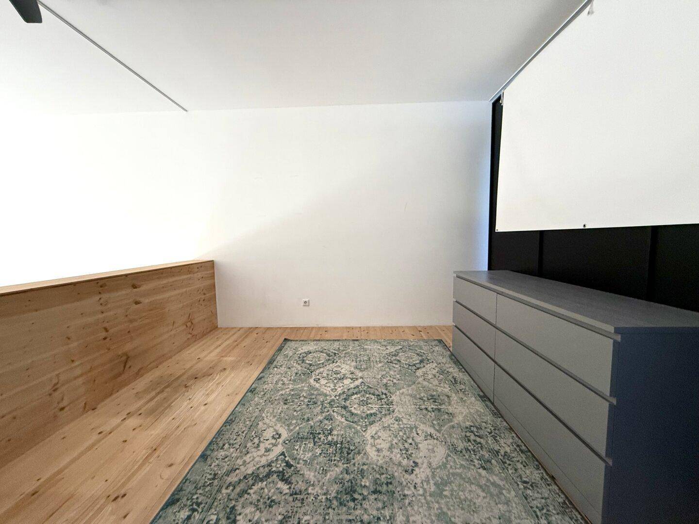 Heller Schlafbereich auf der Galerie mit Holzboden, Teppich und minimalistischer Einrichtung.