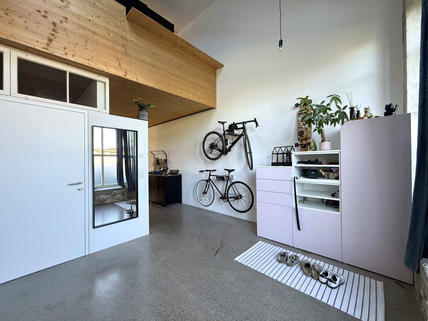 Heller Eingangsbereich mit hohen Decken, Fahrrädern und einem Spiegel in Loft-Atmosphäre.