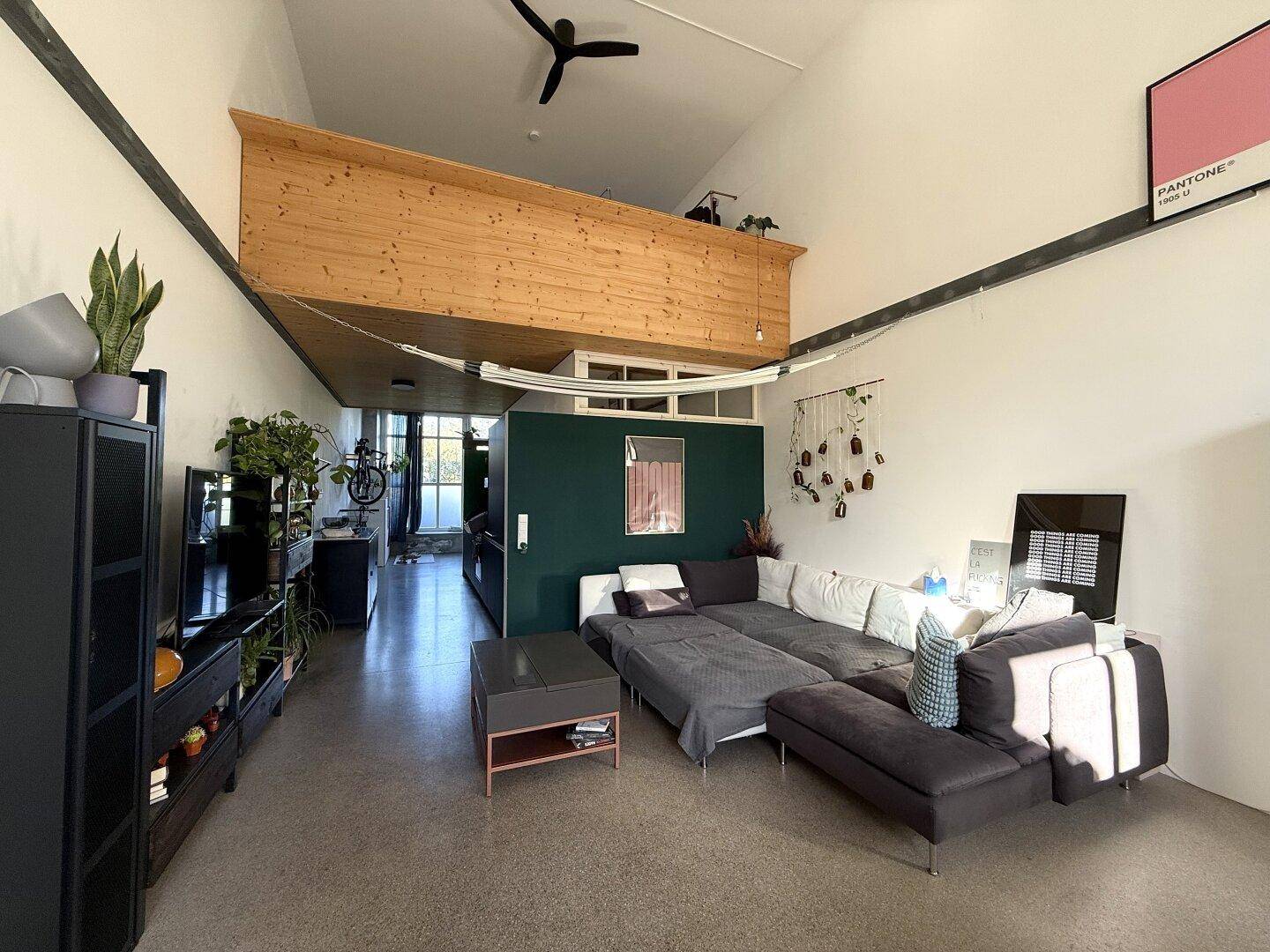 Geräumiges Loft-Wohnzimmer mit hoher Decke, Hängematte und Galeriebereich aus Holz.