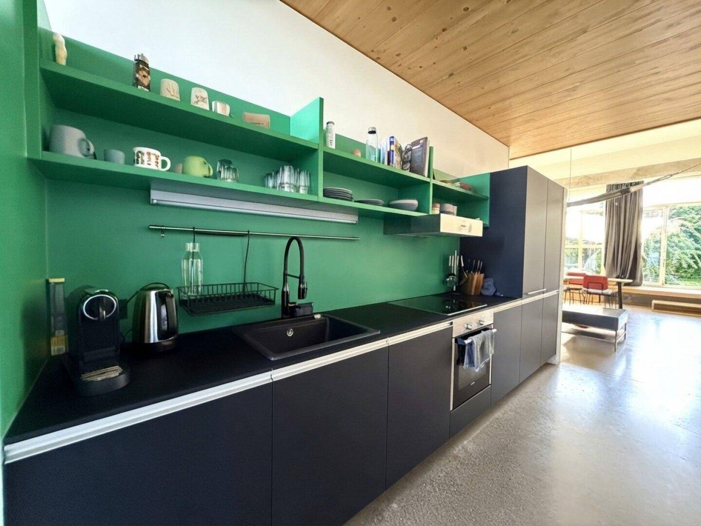 Moderne Küche mit schwarzen Fronten, grünen Regalen, Induktionskochfeld und Holzbalkendecke.