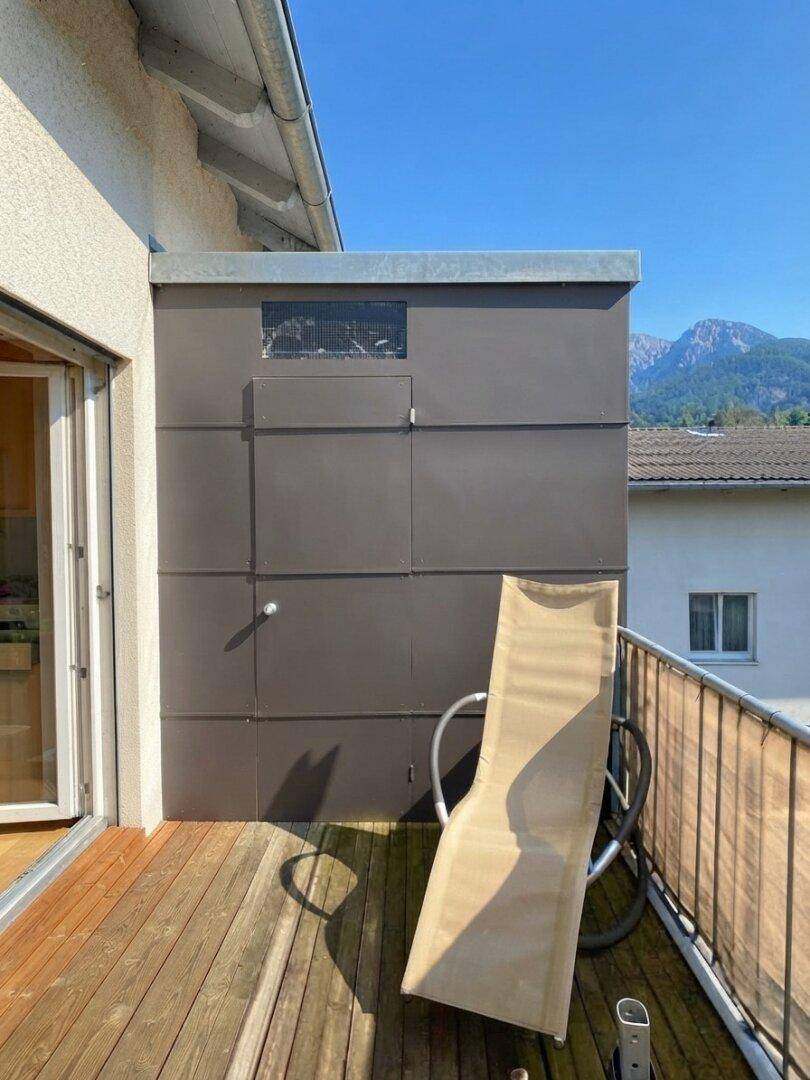 Balkon mit Holzboden, Liegestuhl und praktischem Abstellraum an der Fassade.