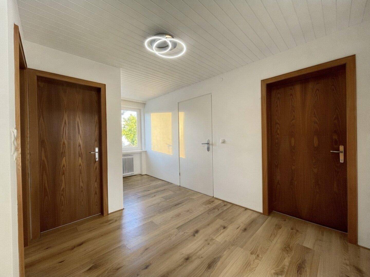 Heller Flurbereich mit Laminatboden, Holztüren und einem kleinen Fenster.