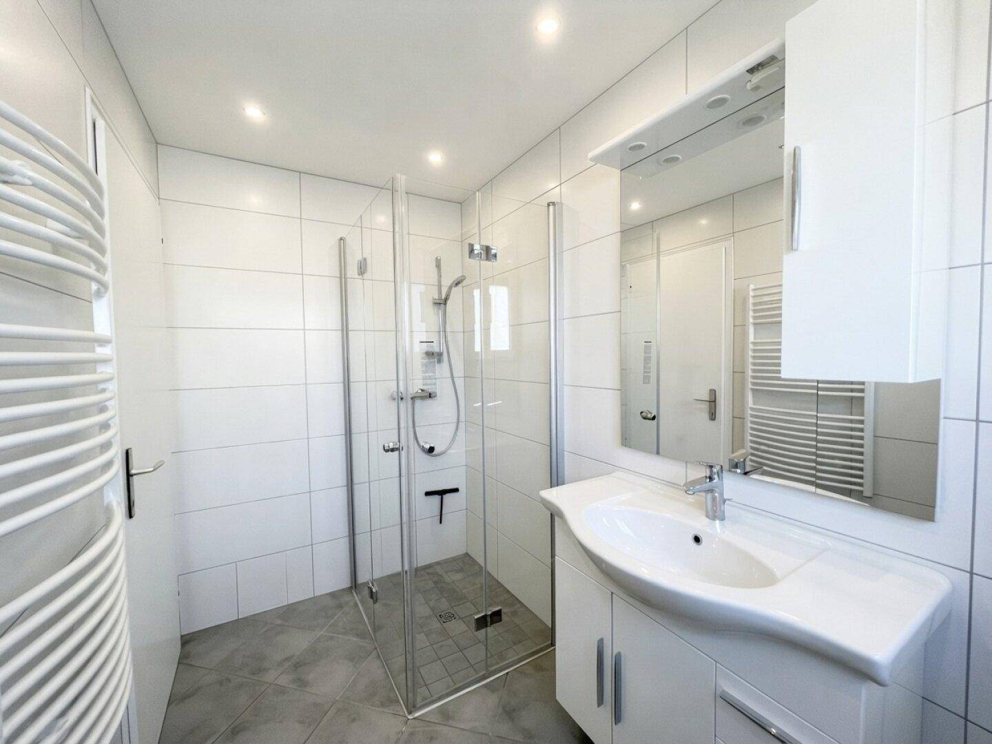 Modernes Badezimmer mit weiß gefliesten Wänden, Glasdusche und beheiztem Handtuchhalter.
