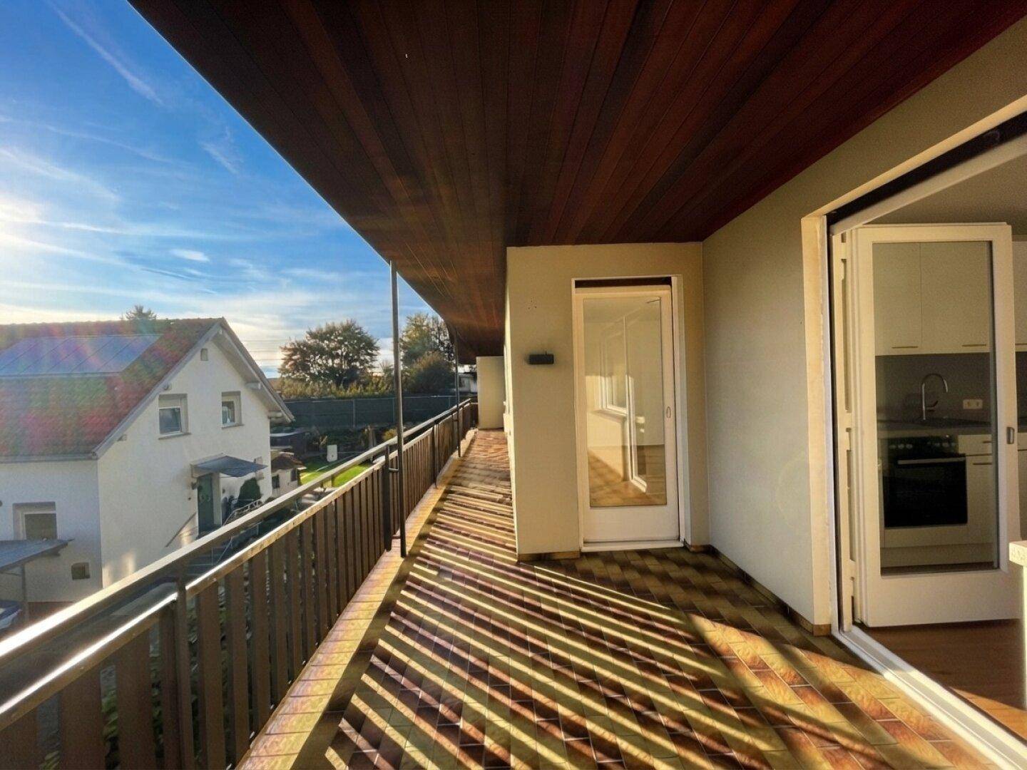 Langer Balkon mit Fliesenboden, Holzdecke und Zugang zu mehreren Räumen.